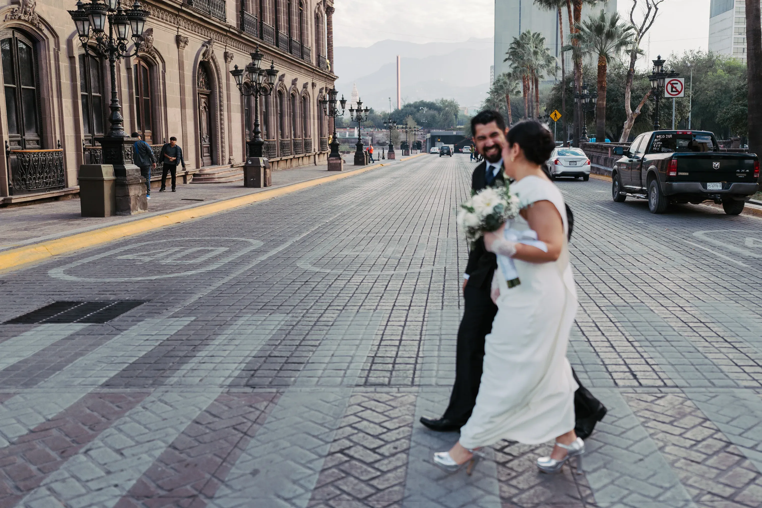 Amy y Jorge cruzando una calle empedrada del centro histórico de Monterrey con las montañas de la Sierra Madre al fondo