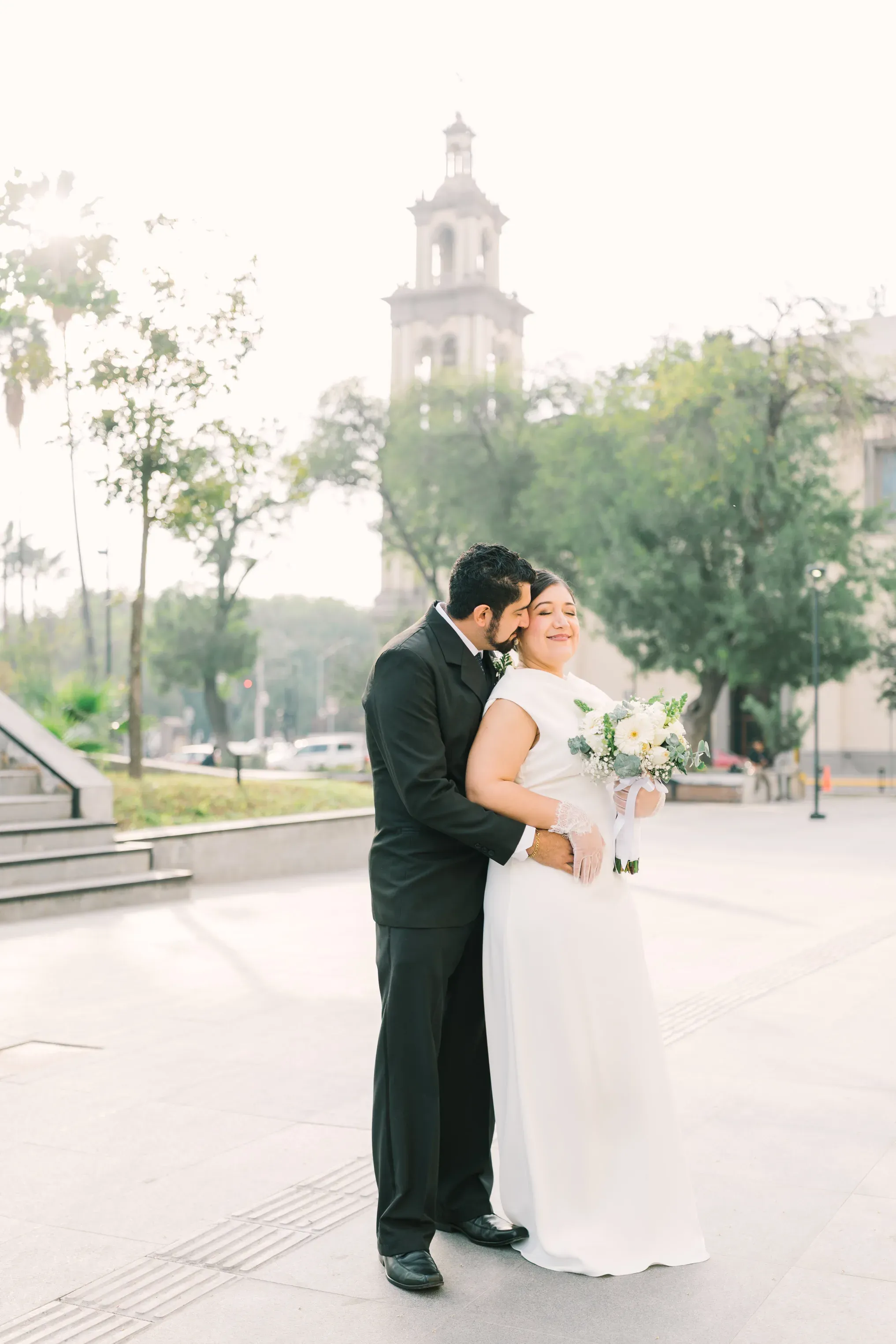Jorge abrazando y besando a Amy sonriente en la Macroplaza de Monterrey con la torre de la iglesia al fondo